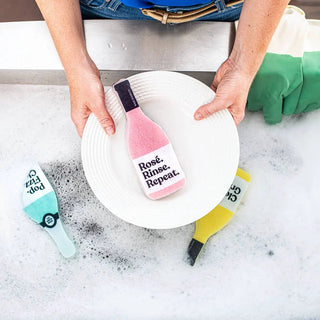 Scrubbly kitchen sponge Rosé Rinse Repeat, pink bottle sponge on a white plate with 3 assorted scrubbies nearby