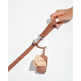 Poop bag carrier dispenser on tan belt strap with a silver clip and attached tan silicone bag holder.