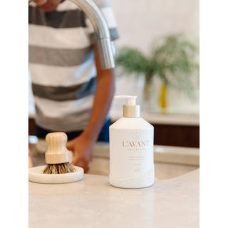 Dish soap bottle with pump, white with gold label, textured base on kitchen counter.