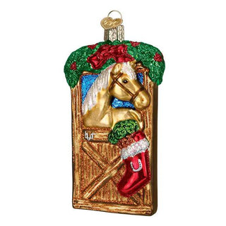 Horse in stall ornament featuring a gold horse in a wooden stall with green garland and red stocking.