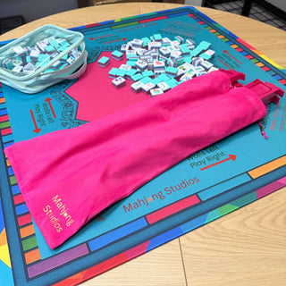 Lunaflor Mahjong Mat with turquoise square tiles scattered on a bright, colorful game mat and a pink carry bag.