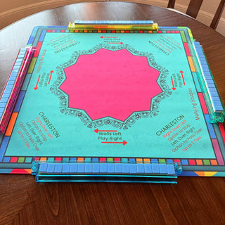 Lunaflor Mahjong Mat with turquoise surface, pink center, ornate border, and three blue-tiled tile racks along the edges.