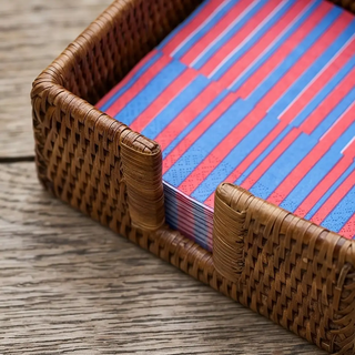 Rattan cocktail napkin holder in natural brown with red and blue striped napkins.