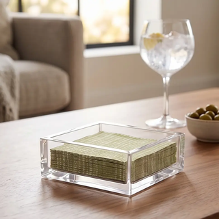 Clear acrylic cocktail napkin holder with stacked metallic-green napkins.