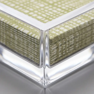 Clear acrylic cocktail napkin holder with green patterned napkins neatly stacked inside