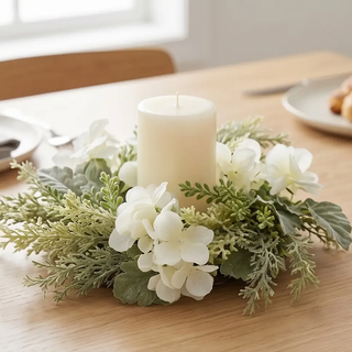 Candle ring with artificial foliage, mixed greenery and white hydrangeas, and a central white pillar candle.