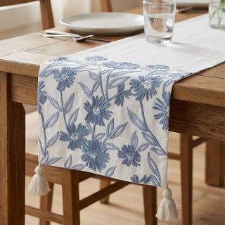72-inch white linen table runner with blue embroidered floral pattern and tassels on ends.