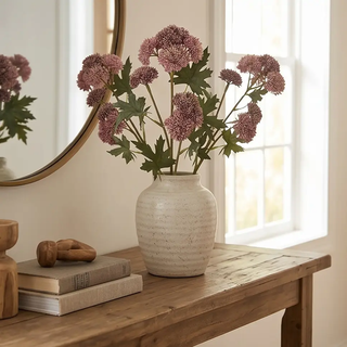 Pink sedum stems artificial plant in a cream ceramic vase on a wooden table