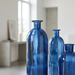 Blue glass bottles, set of three with rounded bodies and narrow necks in a bright room.
