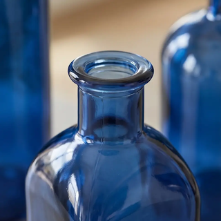 Blue glass bottles with narrow necks, close-up of rims; blue glass bottles in background.