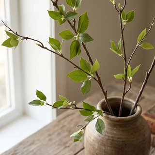 Green leaf branch artificial plant in a rustic ceramic vase on a wooden table