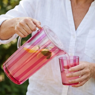 2-1/2 quart acrylic pitcher with fuchsia stripes and lid, pouring into a matching fuchsia tumbler
