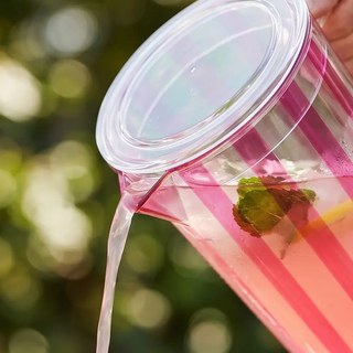 2-1/2 quart acrylic pitcher with fuchsia stripes and lid, pouring water.