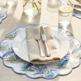 Reversible placemat set of 4 with heron and palm tree motifs, blue scalloped edge, shown under plate with napkin.