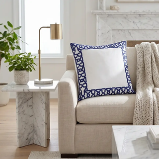 Square white pillow with blue applique border on a beige sofa.