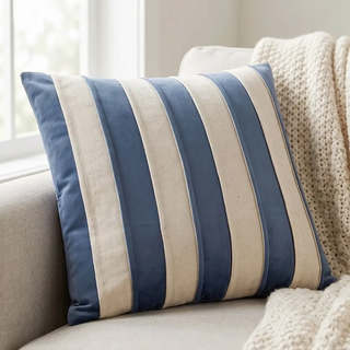 Blue velvet and natural cotton striped square pillow on beige sofa with a chunky knit blanket.