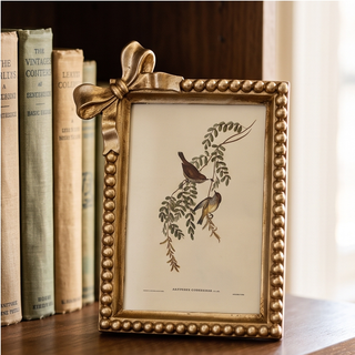 Antique gold bow frame with beaded edge housing a bird-on-branch illustration