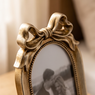 Arched bow frame in gold-tone metal with beaded edge and a large decorative top bow; picture frame.