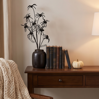 Black glitter spider spray in a dark vase on a wooden desk beside books and a small white pumpkin