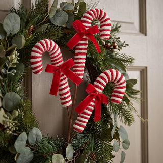Pink peppermint spray candy cane ornaments with red bows on a greenery wreath