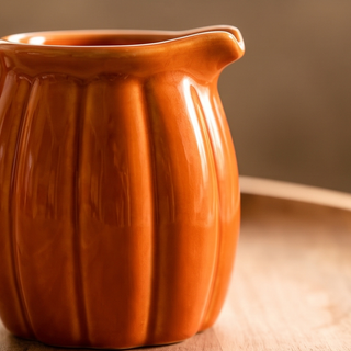 Orange pumpkin-shaped ceramic creamer pitcher with glossy glaze.