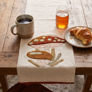 Mushroom dish towel in cream fabric with embroidered mushroom motif and rust pom-pom trim.