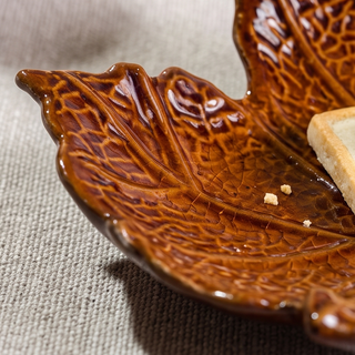 Leaf-shaped burnt brown ceramic plate with a glossy glaze and a few crumbs.