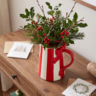 Striped bow pitcher, a red-and-white ceramic serving pitcher filled with holly and pine stems.
