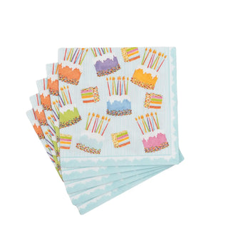 Cocktail napkins with cake frosting designs, candles and sprinkles on pale blue striped paper linen, stacked.