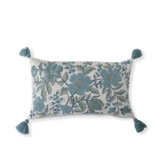 Lumbar pillow with white linen fabric and blue embroidered floral pattern, turquoise tassels at corners.