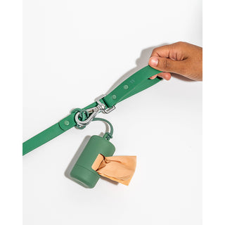 Poop bag dispenser on a green strap with metal hardware, orange bag peeking from the dispenser