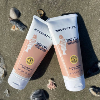 Hand Ritual Favorites Bundle: two peach-colored hand lotion tubes with white caps on a sandy beach.