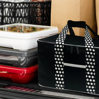 Insulated travel bag in black with white polka-dot handles, placed in a car trunk beside food containers.