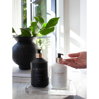 Lucite tray - Medium with two pump bottles (black and white) on a marble surface beside a green plant.