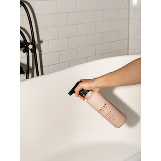 Multipurpose cleaner bottle in blush pink with a black spray nozzle being sprayed into a white bathtub.