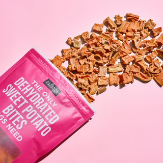 Dehydrated sweet potato bites dog treats in pink packaging with brand label and scattered chunks