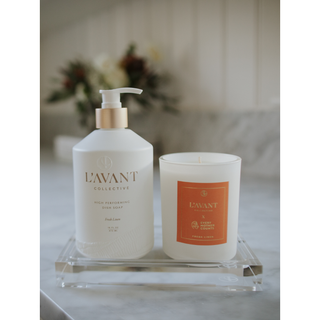 Lucite tray with a white pump soap bottle and orange-labeled candle on a marble surface