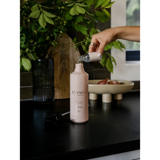 Multipurpose cleaner in blush pink on a kitchen counter as a hand pours from a labeled bottle.
