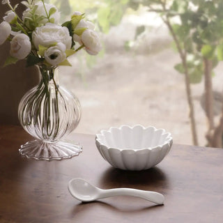 White Vienna mini bowl with spoon; scalloped edge, beside a clear ribbed glass vase with white flowers.