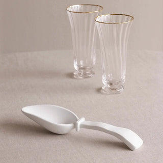 White ice scoop with curved handle; two clear glass goblets with gold rims sit on a neutral table in the background