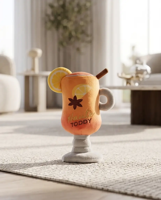 Haute Toddy dog toy; orange gradient plush cocktail with lemon slice, cinnamon stick, and gray pedestal base.