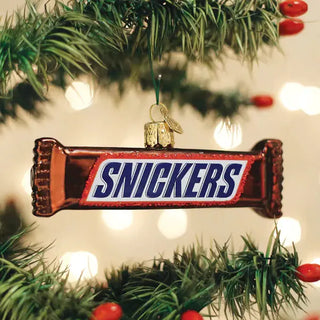 Snickers ornament, candy-bar shaped with metallic red wrap, hanging on a Christmas tree.