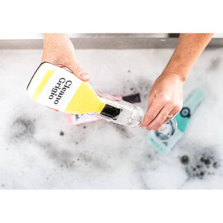 Scrubbly kitchen sponge Cleano Grigio held in hands with foamy water and a turquoise dish scrubber nearby