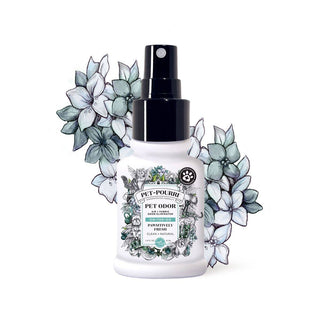 Pet odor eliminator spray bottle, white container with black spray cap, ornate illustrated label, blue floral backdrop