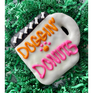 Dog bone-shaped dog treat cake with white icing, orange DOGGIN, pink DONUTS, black bone-band
