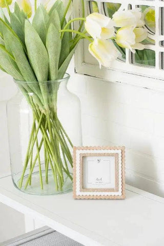 Wood scallop photo frame for 4x4, natural/white, on a white shelf beside a vase of yellow-white tulips.