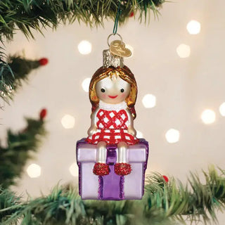 Misfit Doll Ornament on a Christmas tree, red plaid dress, gold hair, silver crown, perched on a purple gift box.
