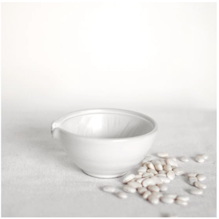 Decorative ceramic bowl, white glazed finish, on a light surface with white beans beside.