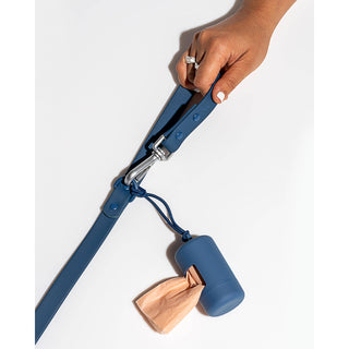 Poop bag carrier dispenser in blue attached to a dog leash, peach waste bag visible