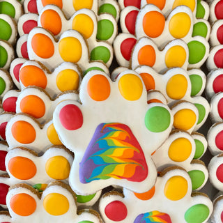 Pride Paw bone-shaped cookie with white icing and rainbow paw pad design, many pieces.